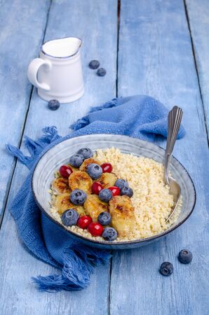 Wheat porridge with fruit and berries in a dish on a wooden background. Selective focus.の写真素材
