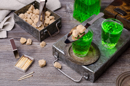 Green liquid in a glass with sugar cubes on a dark wooden background. Selective focus.