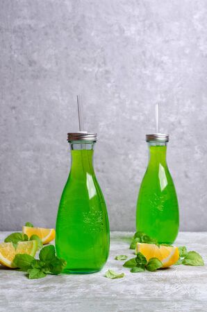 Green liquid in a glass bottle on a slate background with lemon and basil. Selective focus.の写真素材