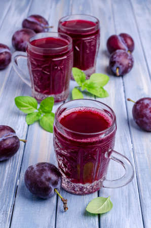 Red plum juice in glass on a blue wooden background with fresh fruit. Selective focus.の写真素材