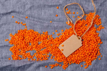 Dry red lentils on a blue textile background with an empty sticker. Top view. Design concept. Copy space.の写真素材
