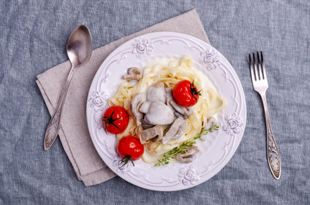 Traditional pasta with mushrooms and tomatoes in a white sauce in a dish on a blue textile background. Selective focus.の写真素材