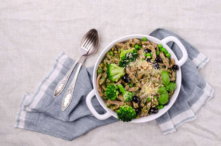 Traditional brown pasta with green vegetables, olives and pesto sauce. Overhead view. Selective focus.の写真素材
