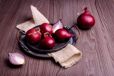 Raw red onion in a metal plate on a dark wooden background. Selective focus.の写真素材