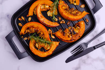 Baked pumpkin slices with seeds and rosemary on a dark baking sheet. Selective focus.の写真素材