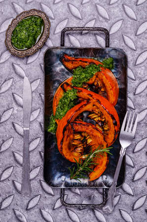 Baked pumpkin slices with green sauce in a plate on a metal background. Selective focus.の写真素材