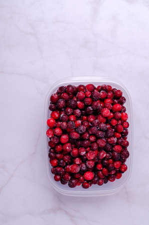 Frozen cranberries in a plastic container on a marble background. Selective focus.の写真素材