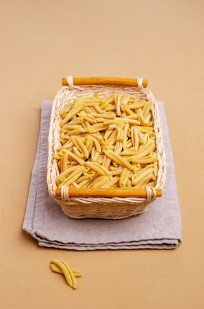 Yellow dry pasta in a wicker basket on a light stone background. Selective focus.の写真素材