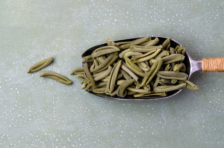 Green dry pasta in a metal scoop on a light stone background. Selective focus.の写真素材
