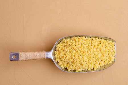 Fine dry pasta in a metal scoop on a light brown background. Selective focus.