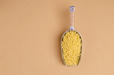 Fine dry pasta in a metal scoop on a light brown background. Selective focus.の写真素材