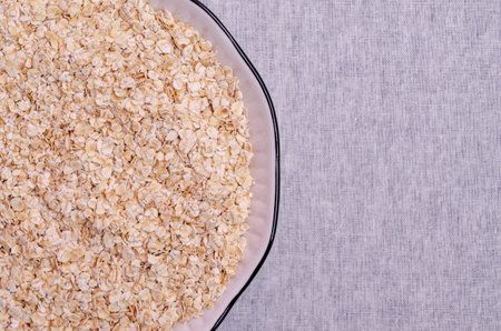 Dry oat flakes in a ceramic dish on a textile background. Selective focus.