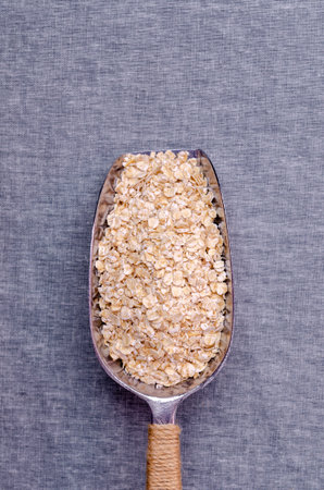 Dry oat flakes in a metal scoop on a textile background. Selective focus.