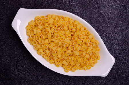 Dry pasta in a ceramic dish on a black background. Selective focus