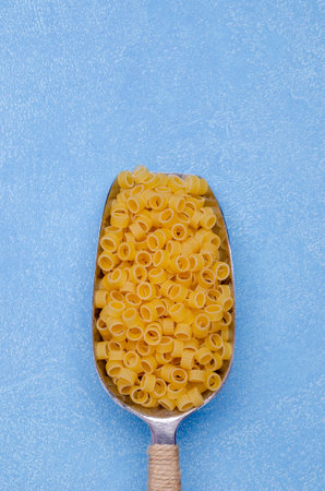 Dry pasta in a metal scoop on a blue background. Selective focus.