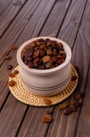 Dark raisins in a wooden dish on a wooden background. Selective focus.