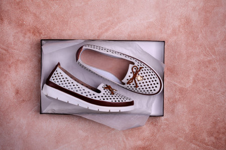 Light women's shoes with a bow and perforation on a brown background. Design concept. A copy of the space. Selective focus.の写真素材