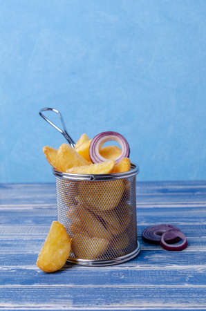 Fried potato wedges in a metal basket on a blue background. Selective focus.の写真素材