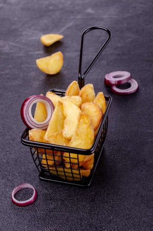 Fried potato wedges in a metal basket on a black background. Selective focus.の写真素材
