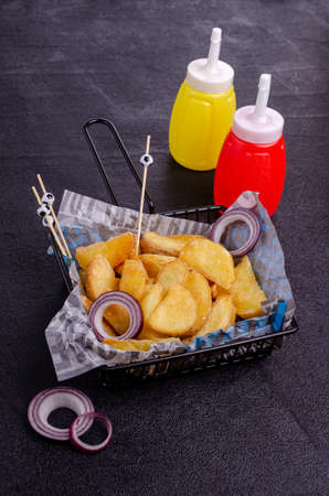 Fried potato wedges in a metal basket on a black background. Selective focus.の写真素材