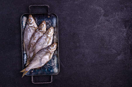 Dried fish on a metal plate on a black background. Top view.の写真素材