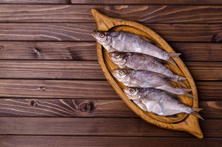 Dried fish on a wooden plate on a dark wooden background. Top view.