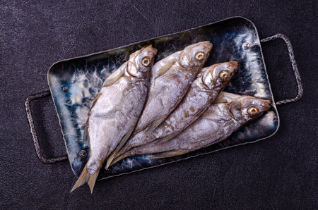 Dried fish on a metal plate on a black background. Top view.