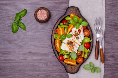 Salad of fresh vegetables. Yellow and red tomatoes, green peppers, capers, basil and feta cheese with spices. Wooden background. Top view.の写真素材