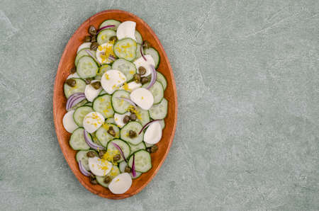 Salad of cucumbers, cheese, capers and lemon zest on a green background. Top view. Selective focus.の写真素材