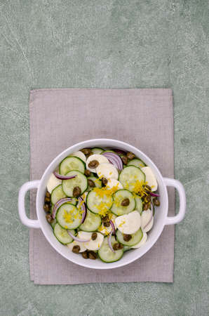 Salad of cucumbers, cheese, capers and lemon zest on a green background. Top view. Selective focus.の写真素材