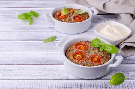 Buckwheat casserole with tomatoes and basil on a wooden background. Selective focus.の写真素材