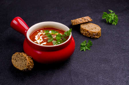 Red puree soup with cream, oil and parsley leaves on a black stone background. Selective focus.の写真素材