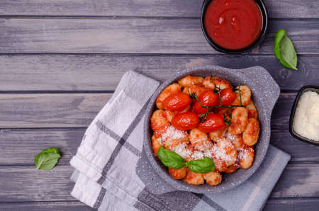 Gnocchi with tomatoes, red sauce, cheese and basil leaves on a gray wooden background. Top view. Selective focus.の写真素材