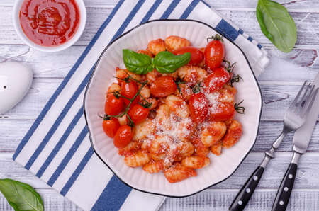 Gnocchi with tomatoes, red sauce, cheese and basil leaves on a light wooden background. Top view. Selective focus.の写真素材
