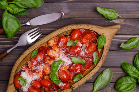 Gnocchi with tomatoes, red sauce, cheese and basil leaves on a brown wooden background. Top view. Selective focus.の写真素材