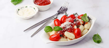 Gnocchi with tomatoes, red sauce, cheese and basil leaves on a marble background. Selective focus. Top view.の写真素材