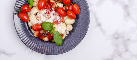 Gnocchi with tomatoes, red sauce, cheese and basil leaves on a marble background. Selective focus. Top view.の写真素材