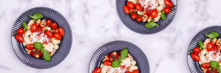 Gnocchi with tomatoes, red sauce, cheese and basil leaves on a marble background. Selective focus. Top view.の写真素材