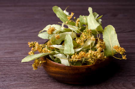 Dried linden leaves and flowers in a bowl. Wooden background. Design concept. Selective focus.の写真素材