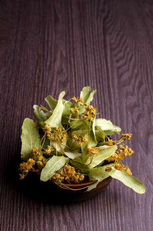Dried linden leaves and flowers in a bowl. Wooden background. Design concept. Selective focus.の写真素材