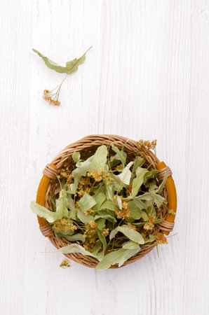Dried linden leaves and flowers in a wicker basket. Wooden background. Design concept. Selective focus.の写真素材