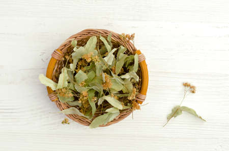 Dried linden leaves and flowers in a wicker basket. Wooden background. Design concept. Selective focus.の写真素材