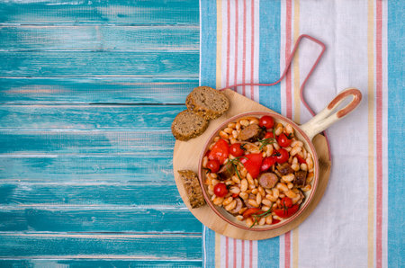Braised beans with vegetables and fried sausages on a wooden background. Top view.の写真素材