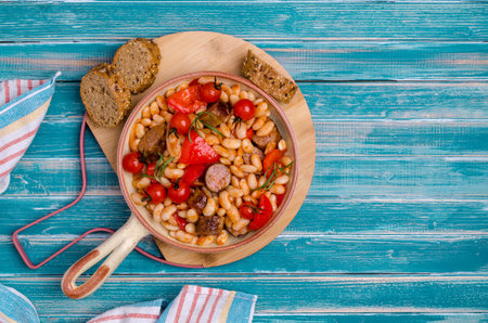 Braised beans with vegetables and fried sausages on a wooden background. Top view.の写真素材