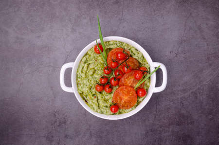 Spicy green mashed potatoes with fried tomatoes in a ceramic dish on a dark background. top view.の写真素材