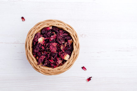 Dried hibiscus petals in a wicker basket on a light wooden background. top view. copyspace.