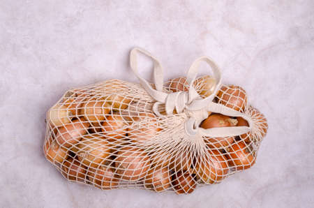 Fresh yellow onions in a knitted bag on a light background. The concept of zero waste. top view. A copy of the space.の写真素材