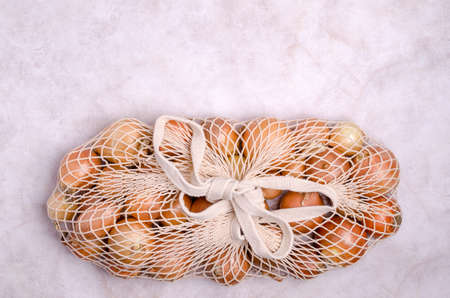 Fresh yellow onions in a knitted bag on a light background. The concept of zero waste. top view. A copy of the space.の写真素材