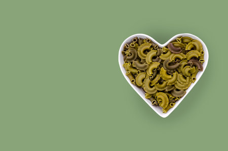 Green dry organic pasta. In a ceramic dish on a green background. top view.