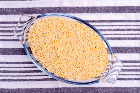Dry risoni pasta in a glass jar on a light background. top view.の写真素材